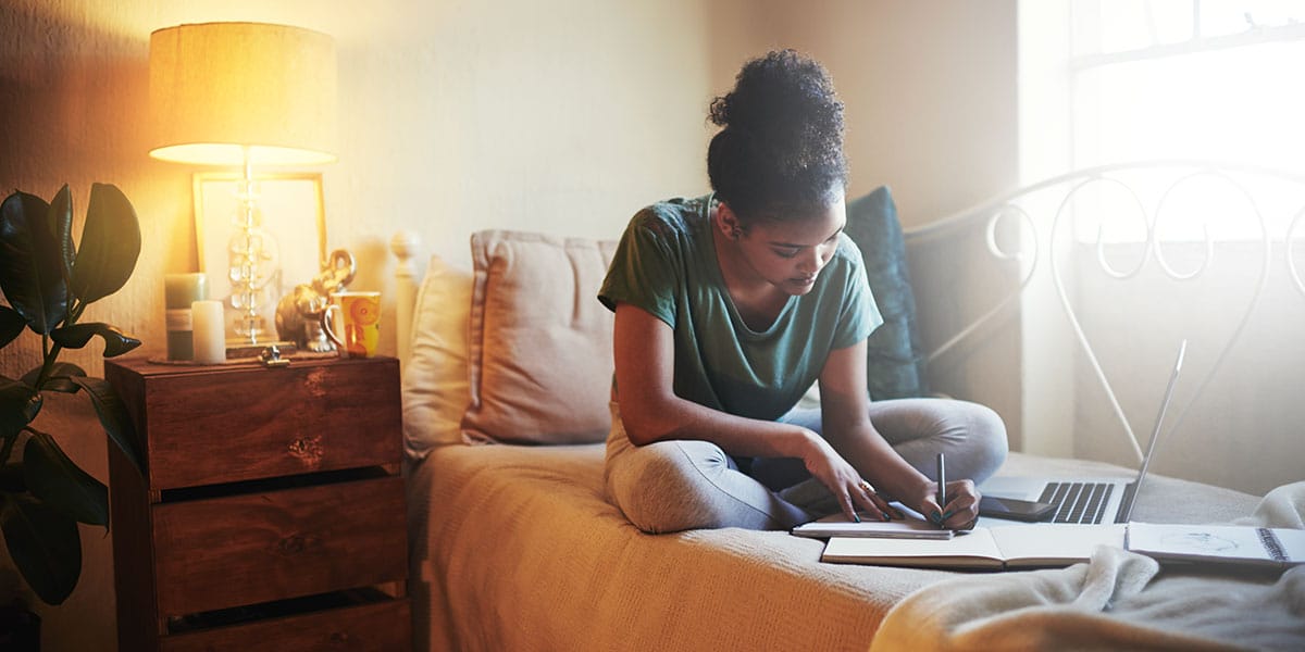 Young woman studying and sitting on her bed